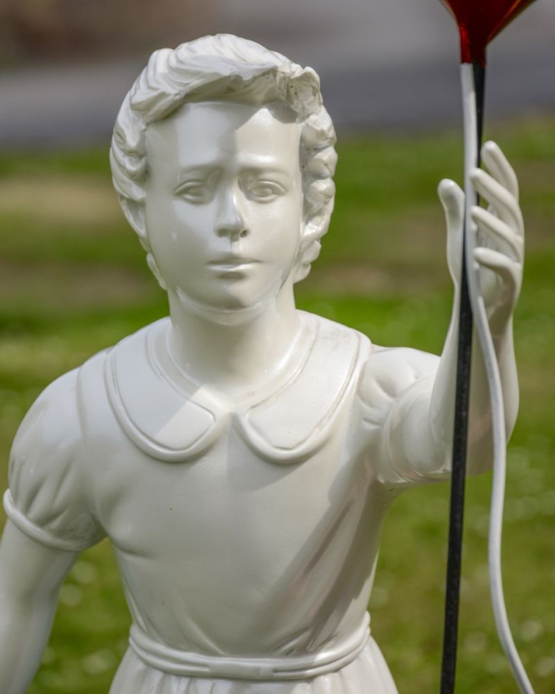 Detailed close-up of the white sculpture's face and raised hand holding the string of the metallic red heart balloon.