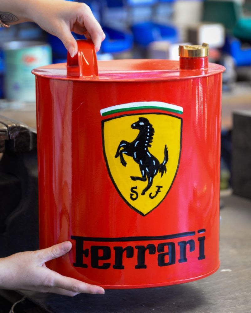 Red, retro, metal Ferrari oil can with hand-painted Ferrari horse shield logo and brass filler cap, front view, being held with two hands for scale
