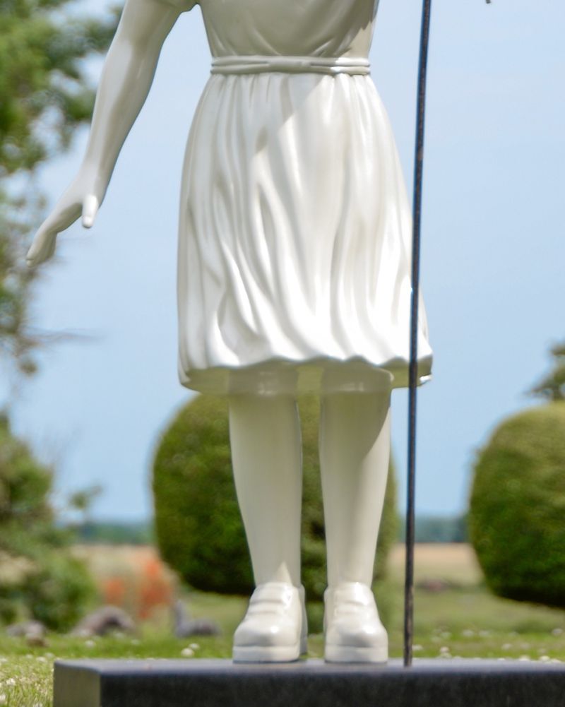 Detailed view of the lower half of the white statue. The dress is pleated and stands on a dark rectangular base.